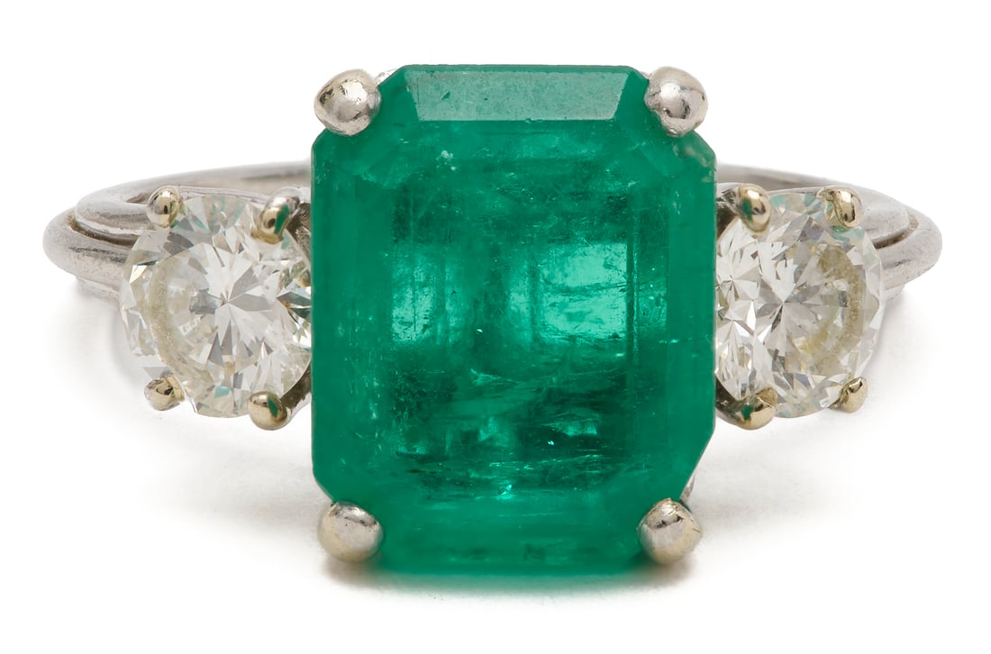 Platinum Emerald and Diamond Three-Stone Ring: Platinum three-stone ring featuring one (1) emerald-cut emerald with an estimated weight of approximately 3.85 carats, enhanced with green oil, flanked by two (2) round brilliant cut diamonds, each ap