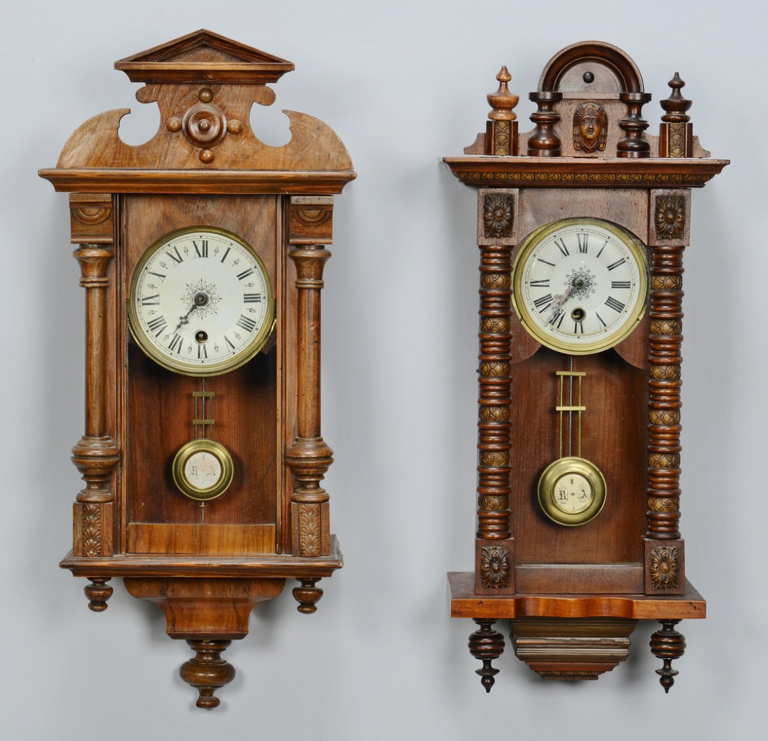 2 Carved Regulator Wall Clocks: Two carved walnut time and strike regulator wall clocks in the Renaissance Revival style, both having porcelain dials with Roman numerals and "R-A" chime pendulums. One clock measures 22 1/2" H x 9 1/