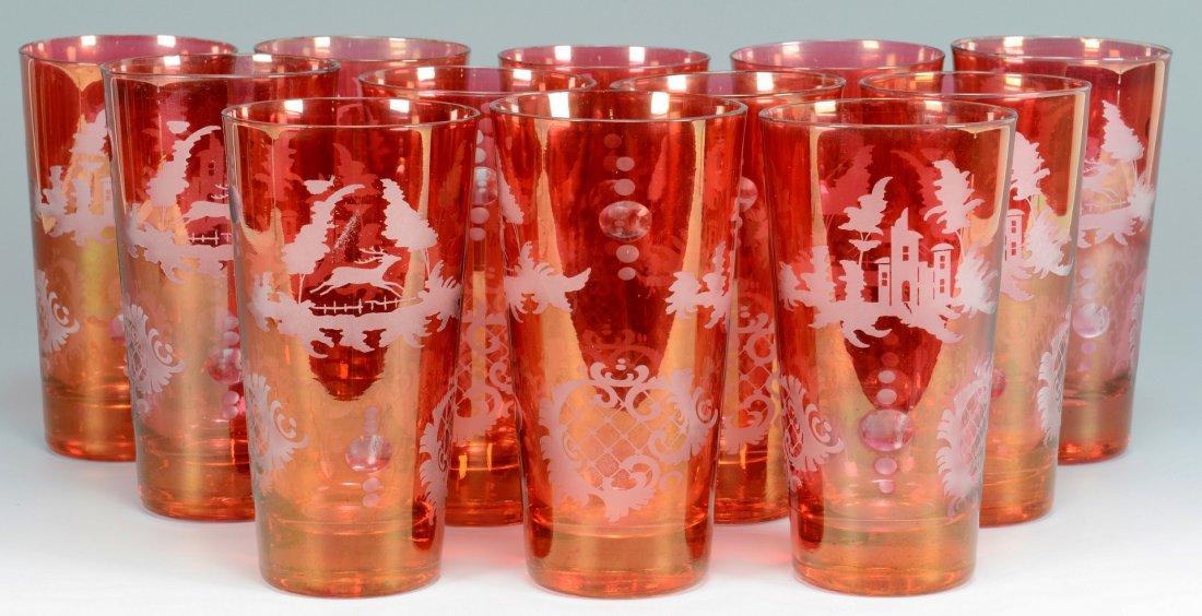 12 Bohemian Cranberry Glass Tumblers: Set of twelve Czech or Bohemian cranberry flashed glass tumblers, with cut-to-clear finger indentions and etched designs including castles, cartouches, and running deer. 6"H. Early 20th century.