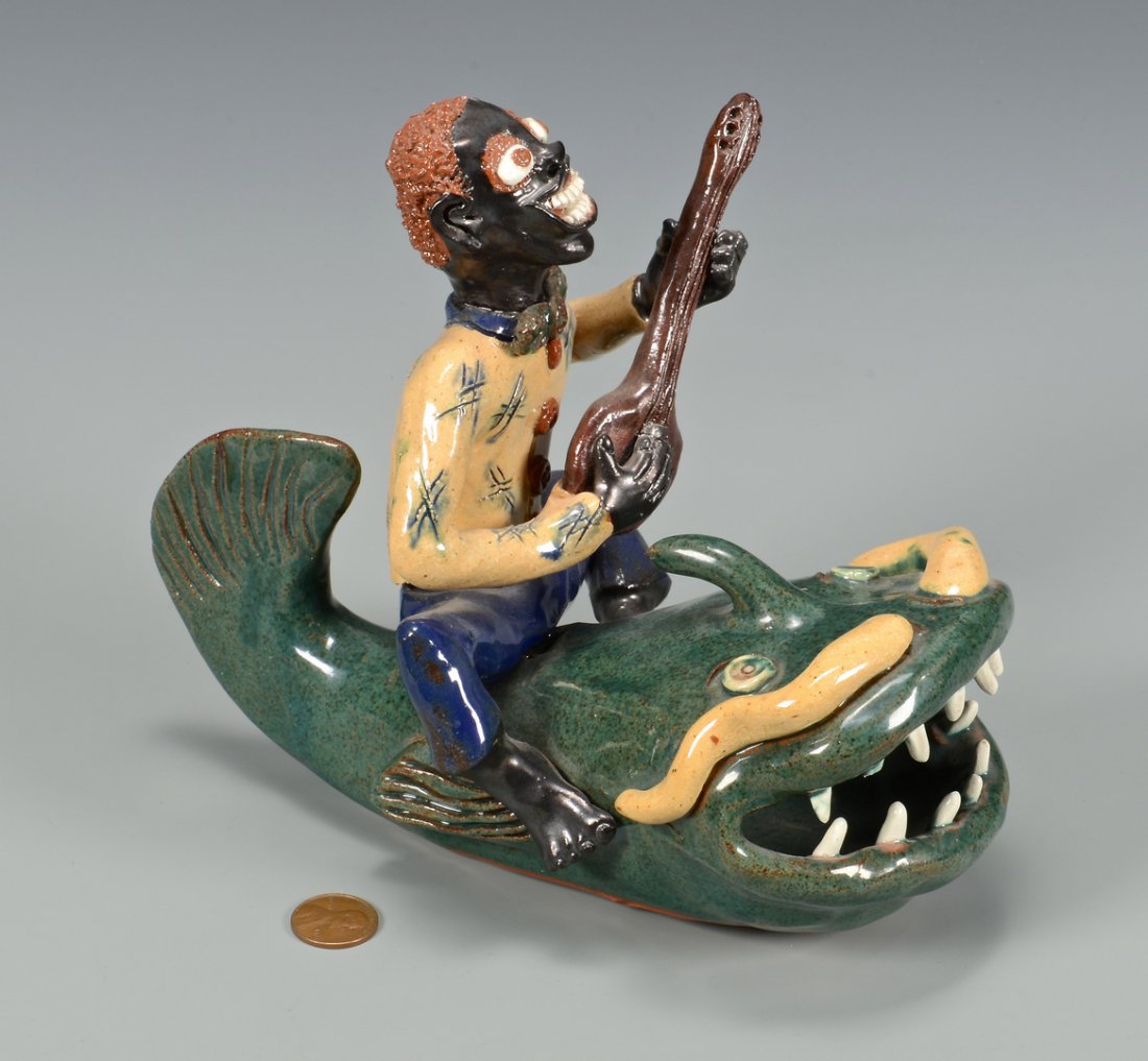 NC Folk Art Figural, Billy Ray Hussey: Southern Folk art pottery figural by Billy Ray Hussey having a polychrome glaze and depicting an African American male strumming a banjo atop a catfish. Signed "BH XX" to base. 6 1/2" H x 8" D x 4" W.