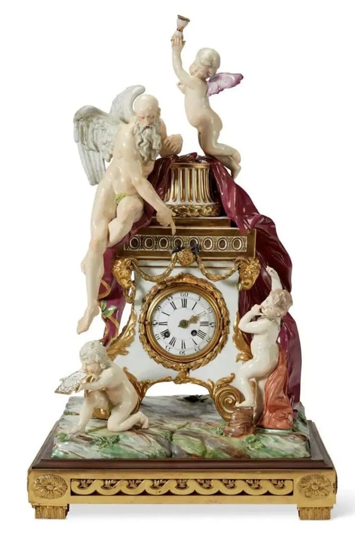 18TH C. VIENNA PORCELAIN FIGURAL MANTEL CLOCK ON AN ORMOLU BASE: The rectangular scroll-footed case surmounted by a fluted column and applied with a large swag of burgundy drapery, the winged and bearded figure of Chronos seated on the left and pointing to the cloc