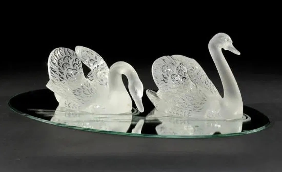 A PAIR OF LALIQUE SWANS ON A MIRROR: stunning pair of Lalique Swans with their original etched plateau. Head up: 13" length by 10" height by 8" width. Head down: 14" length by 7.5" height by 8" width. Plateau: 33" length by 22" width.