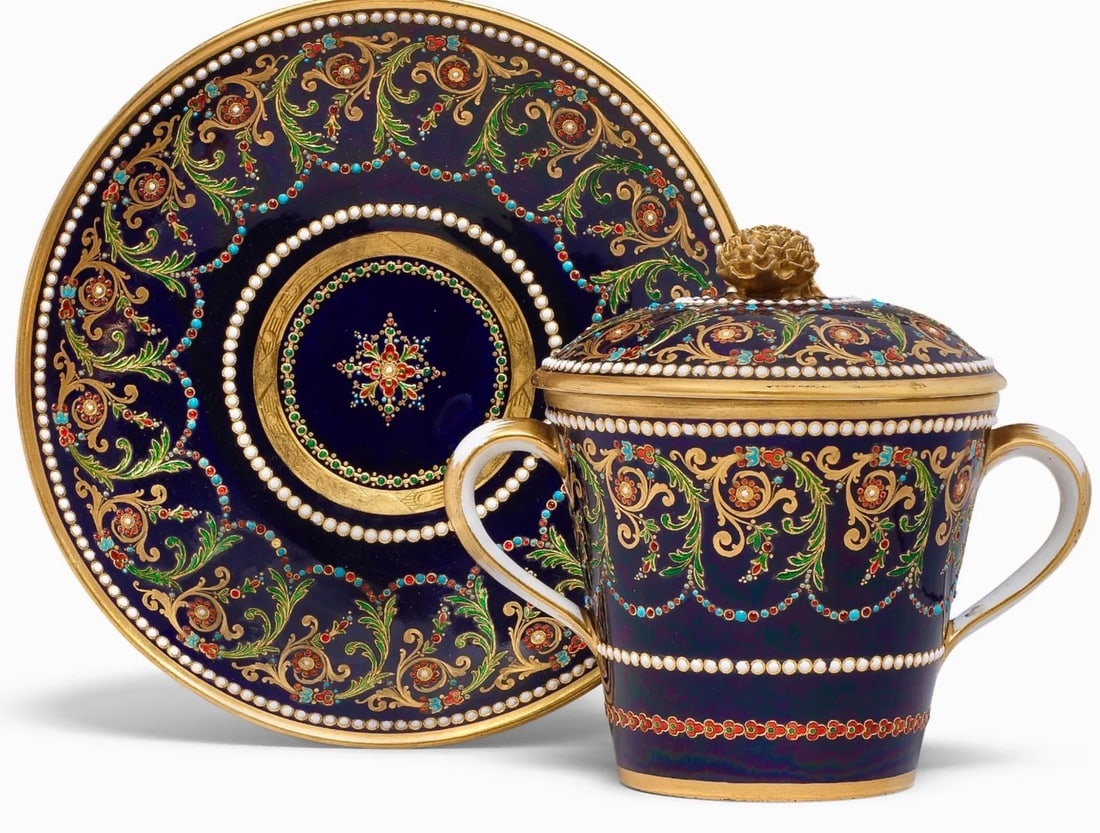 A LARGE SEVRES STYLE CHOCLATE CUP AND COVER AND SAUCER: A Sèvres-style jewelled chocolate cup, cover and saucer, late 19th centuryDecorated with bands of scrolling flowers picked out in bright enamels, between white enamel "jewelled" borders, all against