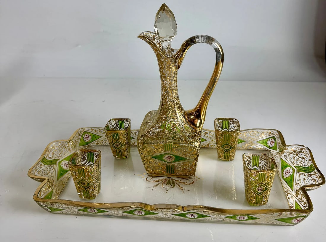 GILT AND ENAMELLED MOSER LIQUOR SET: Circa 1900. Comprising tray, bottle and 4 shot glasses.Tray: 14 x 6.5 x 1.25 Decanter: 9 x 4 x 3.5 Glasses 2.25 x 1.25 eachIn good condition, no brakes, no chips, minor age related loss of gold.Estima