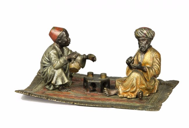 ORIENTALIST COLD PAINTED AUSTRIAN BRONZE GROUP: depicting 2 orientalist men seated on an oriental rug, flanking a low tea table, one is serving tea, the other smoking a pipe, stamped BK and XII, 2.5x5.25in. Estimate $800-1.000