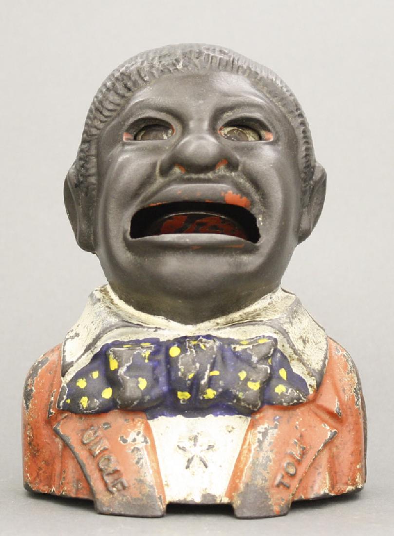 Uncle Tom Iron Bank: Made by Kyser & Rex. Philadelphia, Pa. - Circa 1882. Place a coin on his tongue and press the lever. His eyes will roll and he swallows the coin. Made of Cast Iron. Fine Condition (Replaced Trap).