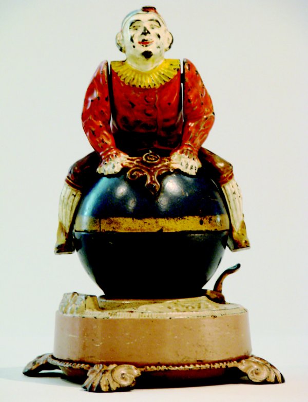 Clown on Globe, Tan Base Mechanical Bank: An iconic bank made by J. & E. Stevens circa 1890. Place a coin in the slot and release the activating lever; the clown spins and flips over and the coin is deposited into the bank. Material: Cast Iro