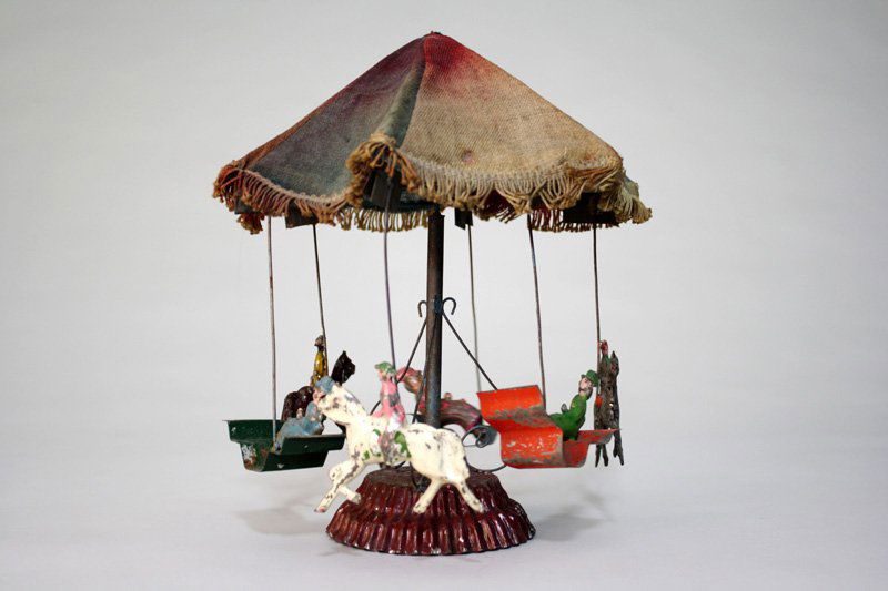 Carousel – Small Wind Up Toy: Germany – Circa 1905 A scarce small version of the classic German carousel with fabric canopy and tin painted figures. In fact, we have never seen this toy before. The toy is 10” tall, 8 ½” wid
