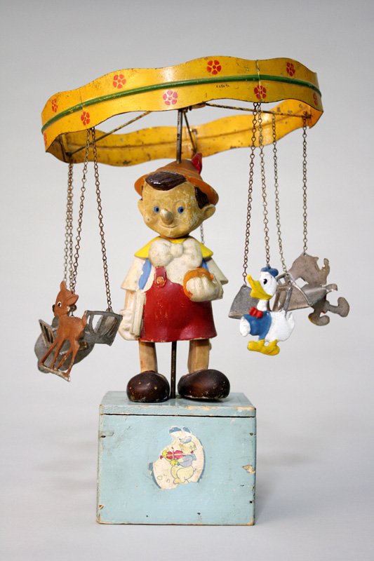 Pinocchio Go Round Wind Up Toy: French/Italian – Circa 1940’s This is an amazing go round with a music box feature. At its center is Pinocchio and the chair go rounds include: Two Donald Ducks, Mickey Mouse, Bambi, and Dumbo. Th