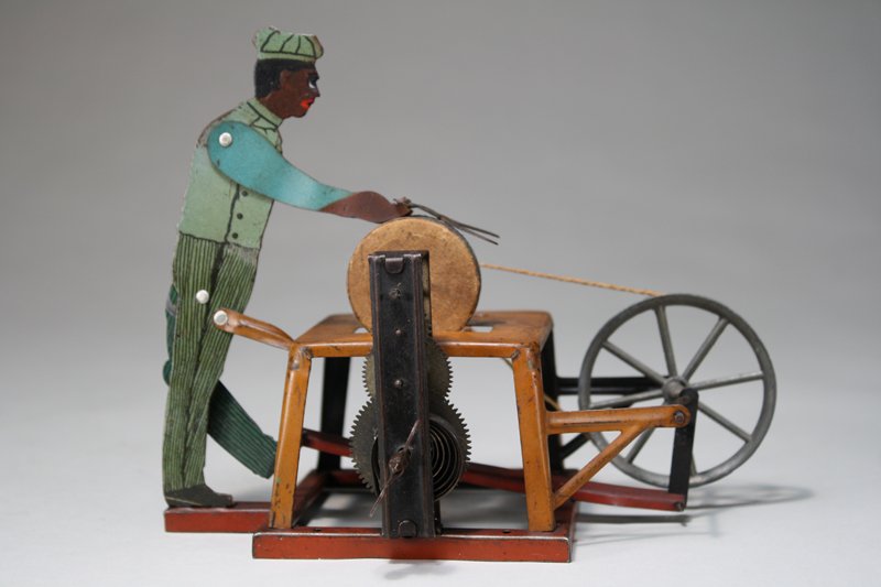 Black Scissors Grinder Windup: Germany – Circa 1925 We have never seen this toy with a black lithographed figure before. It is 7” long and works really well. Material: Tin