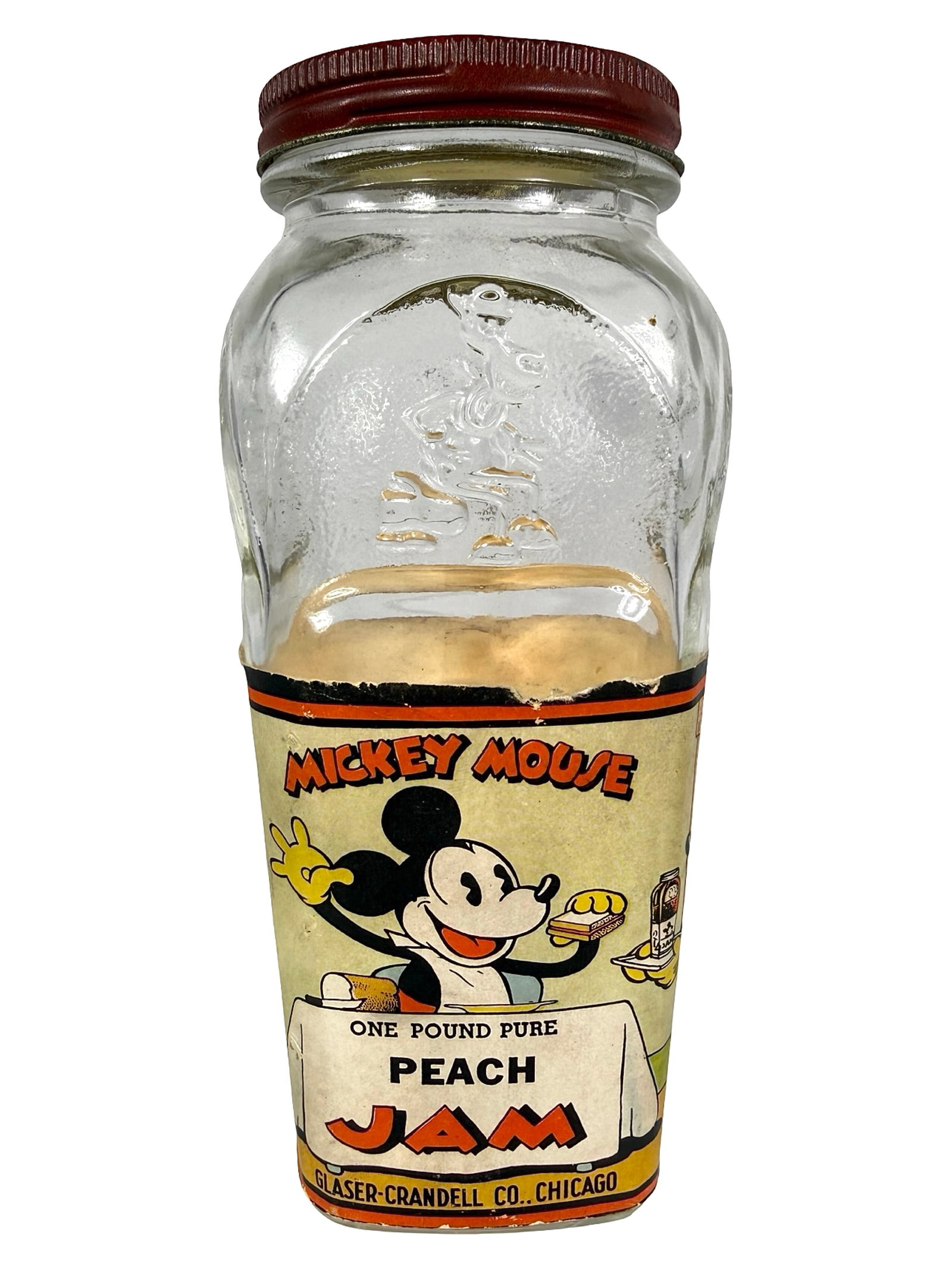 Mickey Mouse Peach Jam Glass & Paper Bank: Made by Glaser - Crandell Co. Chicago, IL - 1930's. 6" Tall x 2 3/4" Wide x 2 3/4" Deep. Bob and Shirley Peirce Collection.