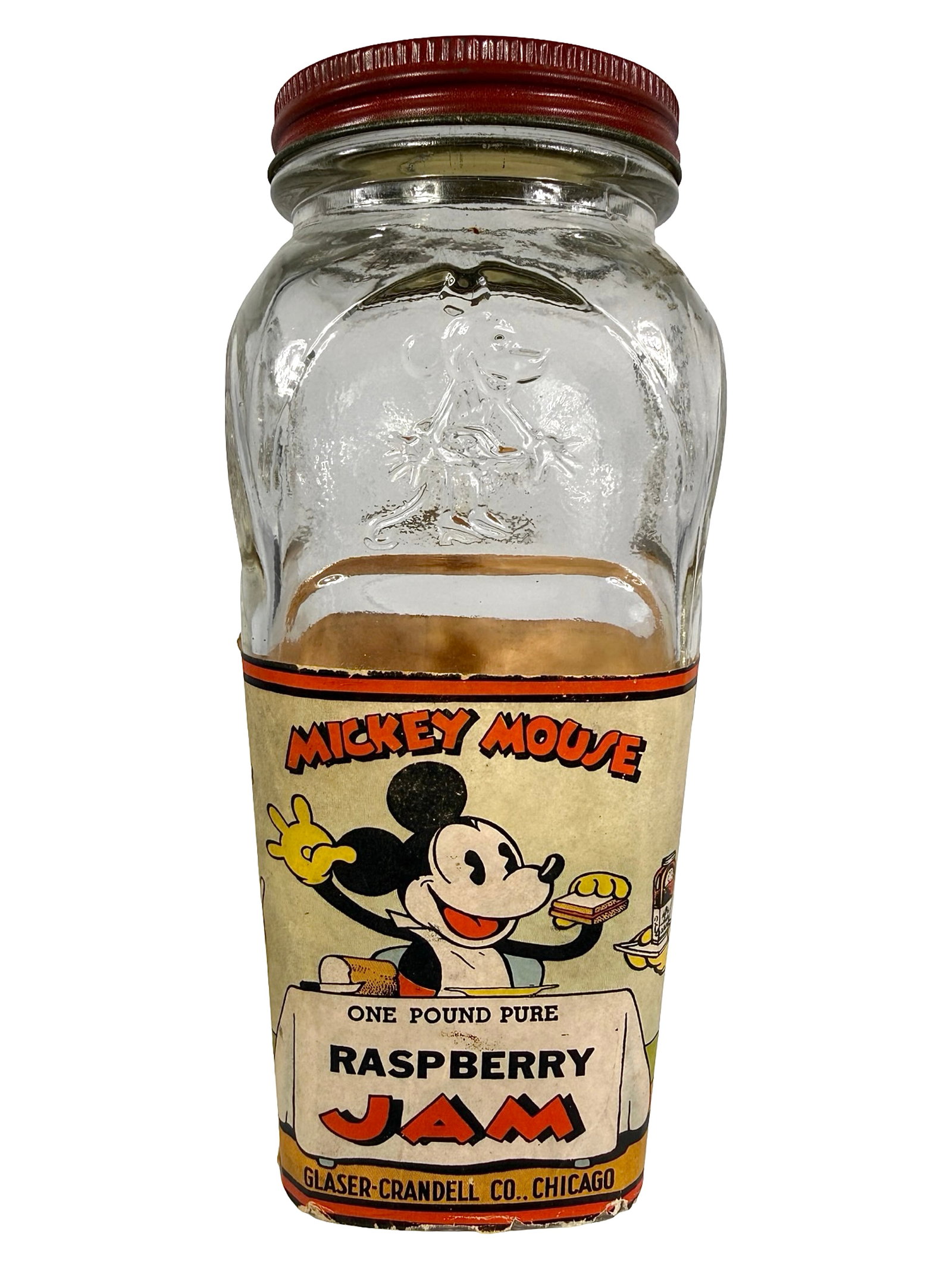 Mickey Mouse Raspberry Jam Glass & Paper Bank: Made by Glaser - Crandell Co. Chicago, IL - 1930's. 6" Tall x 2 3/4" Wide x 2 3/4" Deep. Bob and Shirley Peirce Collection.