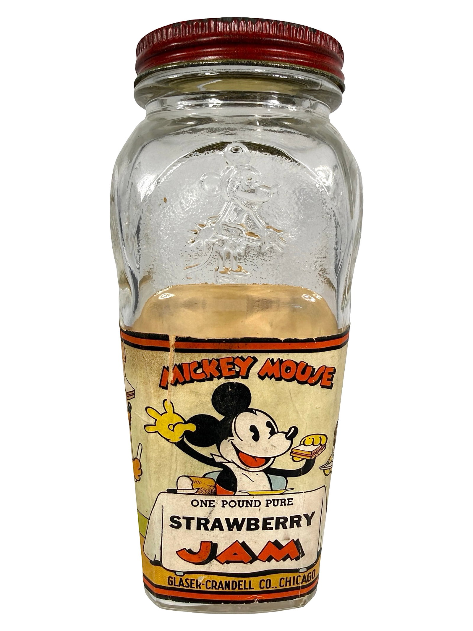 Mickey Mouse Strawberry Jam Glass & Paper Bank: Made by Glaser - Crandell Co. Chicago, IL - 1930's. 6" Tall x 2 3/4" Wide x 2 3/4" Deep. Bob and Shirley Peirce Collection.