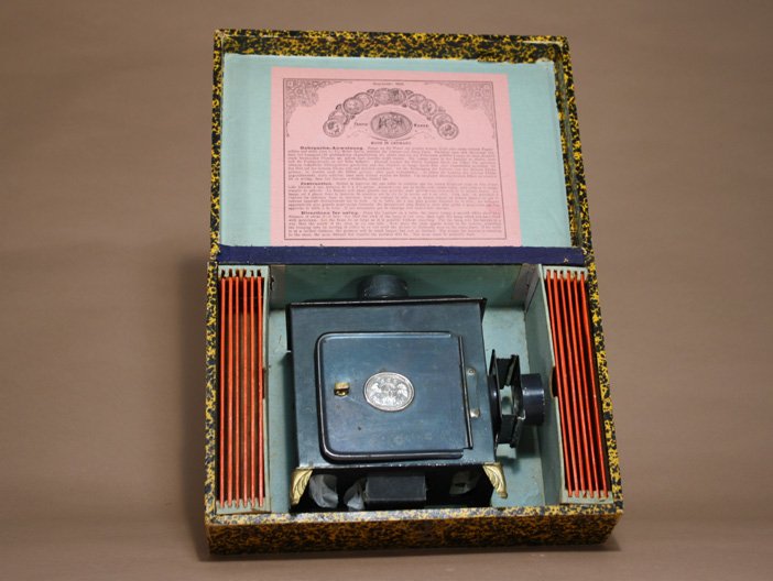 Magic Lantern with Box: Ernst Planck Germany Ð Circa 1890 An early magic lantern in virtually mint in the box condition. It contains 12 colored slides. Material: Tin and Glass