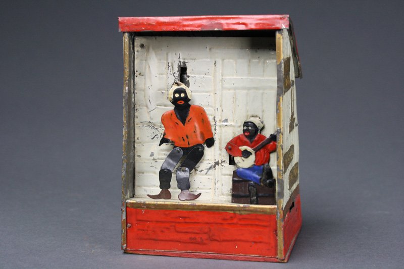 Weedens Plantation - White & Red Mechanical Bank: Made by Weeden Toy Co. Massachusetts – Circa 1887 Wind the mechanism. Drop coin in the slot on the right side of the bank and one man plays the banjo, while the other dances. Material: Tin and Wood