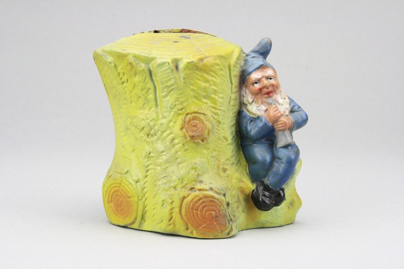 Gnome Playing Instrument: Germany - Circa 1920 This blue dressed sprite plays his tunes in the seclusion of the forest. He is 3.75” tall. Material: Pottery