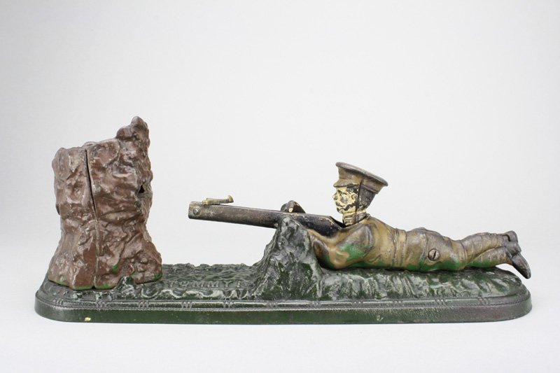 Tommy Bank: John Harper & Company England - Circa 1914 Lay a coin on the rifle after it has been cocked. Press the lever and the coin is shot into the tree. It is a fairly scarce bank. Material: Cast Iron