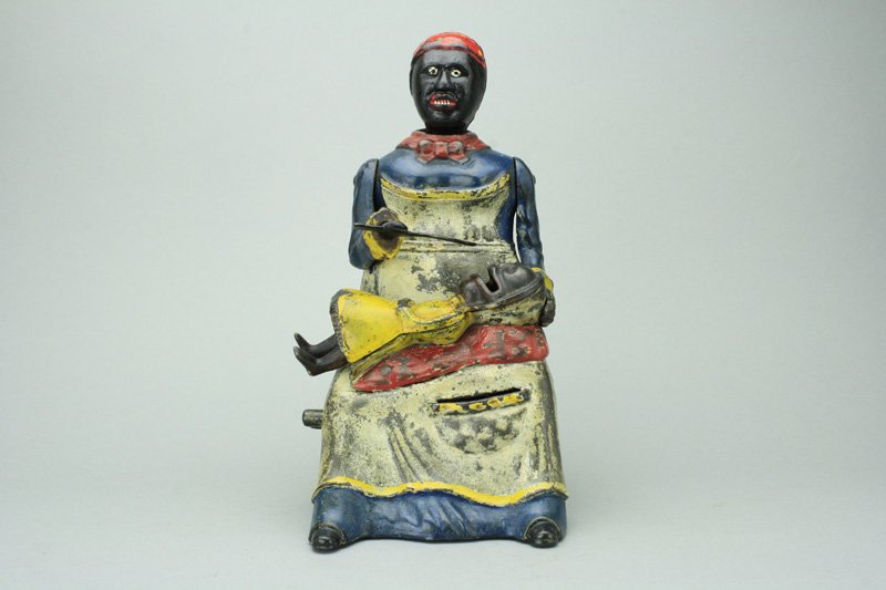 Mammy and Child Bank - Blue Dress: Kyser & Rex Company Philadelphia, Pennsylvania - Circa 1884 Coins can either be fed into the infant’s mouth from Mammy’s spoon or through her apron pocket. Material: Cast Iron