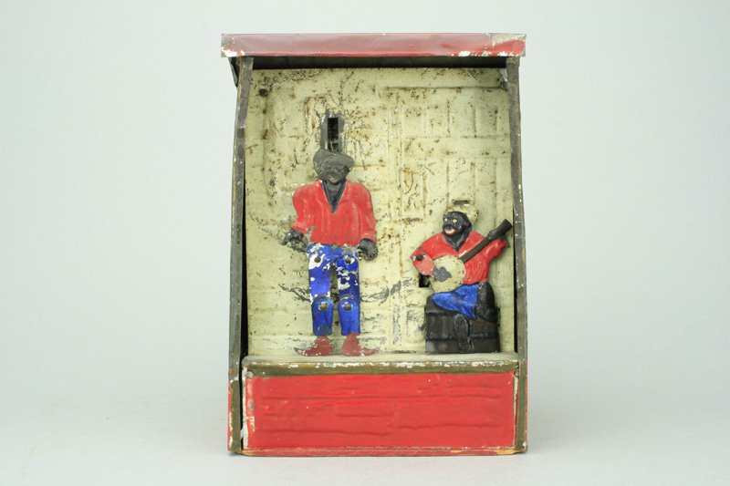 Weedens Plantation: Made by Weeden Toy Co. Massachusetts - Circa 1887 Wind the mechanism. Drop coin in the slot on the right side of the bank and one man plays the banjo, while the other dances. Material: Tin and Wood