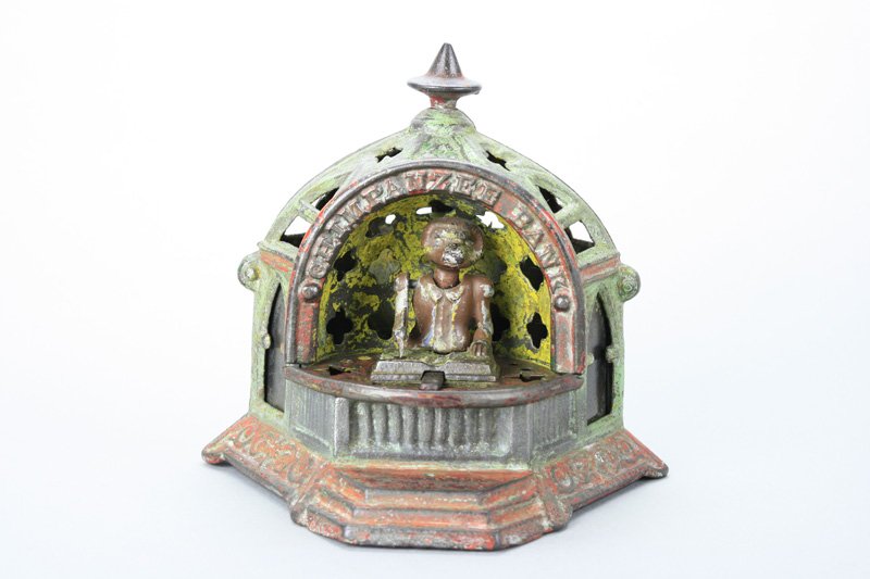 Chimpanzee Bank Mechanical Bank: Made by Kyser & Rex Philadelphia, Pennsylvania - Circa 1880 Move the slide piece toward the monkey’s log book. This causes the coin slot to open and the monkey to lower his arm and head as if he is 