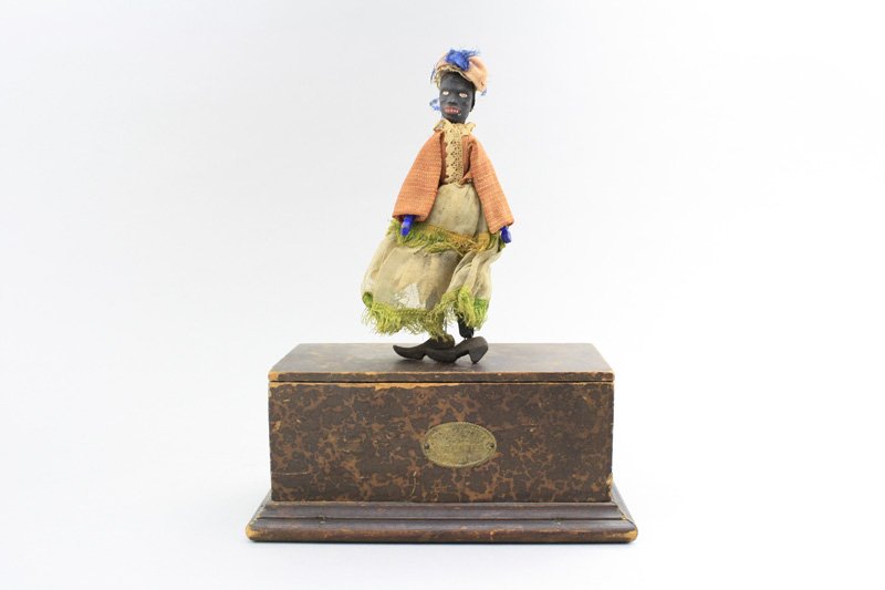 Young Black Woman Jigger: Automatic Toy Works New York - Circa 1867 - 10” Tall This is a scarce toy in wonderful original condition that works well and retains its tin maker’s placard. Material: Papiermache, Fabric and Woo