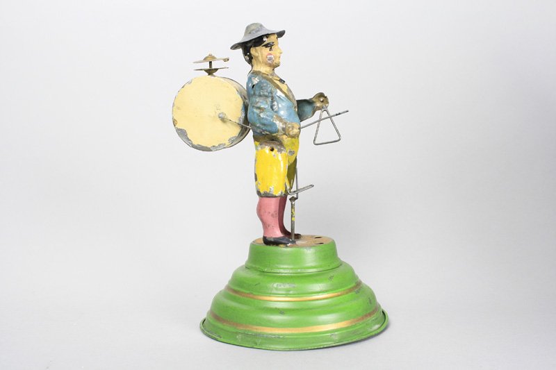 One Man Band on Circular Base: Made by Gunthermann Germany - Circa 1915 - 8.5” Tall This is a scarce and colorful hand painted toy that we have not previously seen. It works well and emits a plinkety-plink sound. Material: Tin