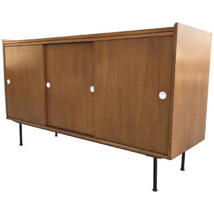 1950s Walnut Credenza after Paul McCobb: A sliding door credenza in the manner of American designer Paul McCobb. Walnut wood with blackened steel legs and white hardware. One section of the piece holds three drawers, the other a shelf. 