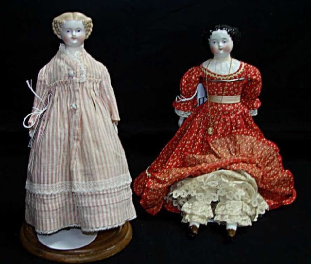 Two "Jenny Lind" Porcelain Dolls: Circa 1860. The doll with dark hair is 12 inches high with china head, hands and feet, appears to have original calico fabric dress. the smaller doll has Parian porcelain head hands and feet. Both dol
