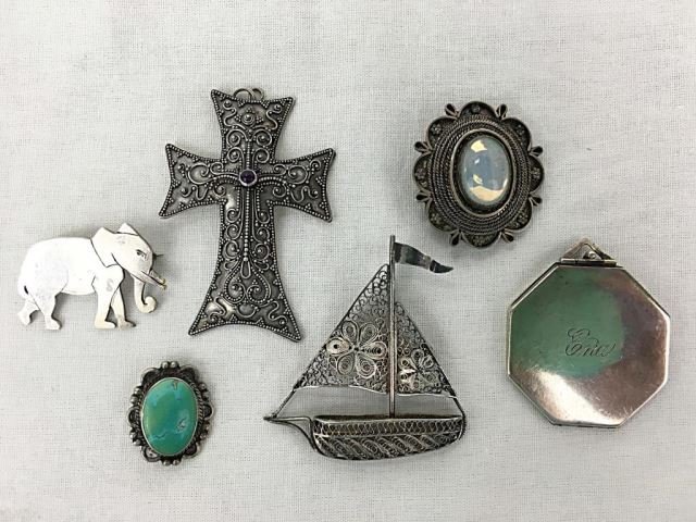 Six Assorted Sterling Pins & Lockets: Six Assorted Sterling Pins & Lockets 55.6 grams total weight size range is 1 - 2.5 inches. Including a cross, filigree sailboat, two ovals set with hard stone, one photo locket, and one elephant pin.