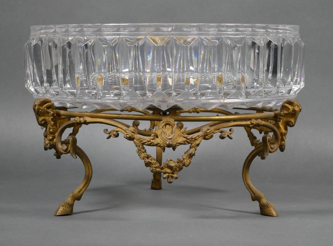 Baccarat Style Cut Crystal Centerpiece Bowl: Baccarat style bronze Ormolu stand with three ram's heads over hoof form feet, below a heavy round cut glass centerpiece bowl with truncated prisms. Overall size is 11" diameter x 7" high.