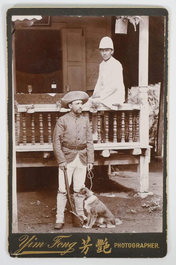 British Indian Army Cabinet Card Photograph: Cabinet card photograph of two soldiers, likely British Indian Army or Colonial Hong Kong. One with rifle and dog, one in white uniform with pith helmet. Photographer is Yim Fong of Hong Kong. Measure