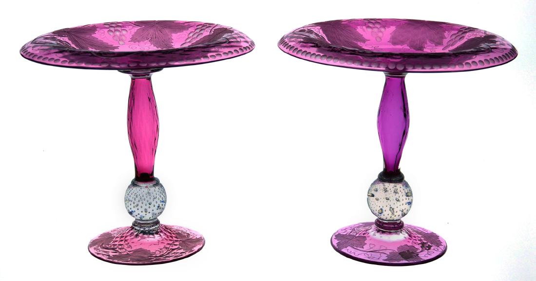 Pair PAIRPOINT Cranberry Art Glass Tazza: Pair of Pairpoint art glass compotes with intaglio grape clusters and vines on a textured surface. Controlled bubbles in the clear ball at the base of the stem. Measures about 8-1/2" diameter and 8-1/