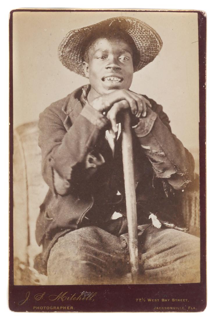Black Americana: Cabinet Photo, Florida Studio: Circa 1880s cabinet photograph of a young African American man wearing a straw hat, and leaning on a walking stick or farm implement. Taken by J.S. Mitchell of Jacksonville, Fla. Photo measures 6-1/2"