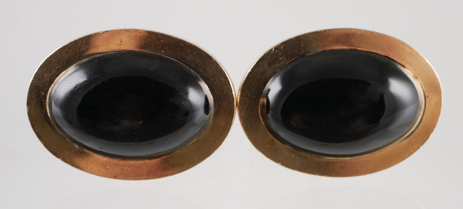 Pair 14K Gold & Black Onyx Cabochon Cufflinks: Pair of 14K yellow gold cuff links by Gump's each with a bezel set, black onyx cabochon. The tops are oval and measure 22 x 16 mm. Each has a hinged bar closure. Marked Gump's, overall weight 13.4 gra