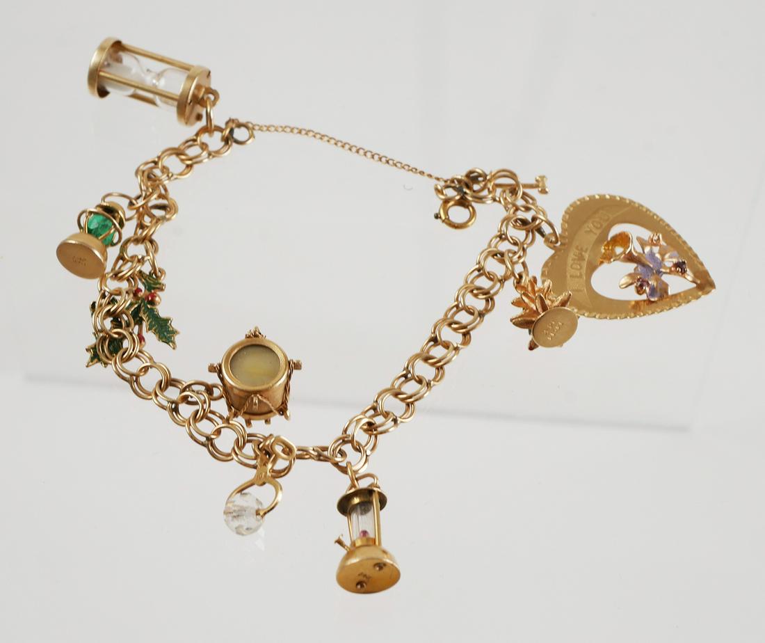Vintage 14K Gold Charm Bracelet: Vintage charm bracelet is set in 14K yellow gold. Charms include: Hourglass, railroad lantern with green stone, holly leaf, drum, ice tongs with crystal, camping lantern, pine tree and "I Love You" he