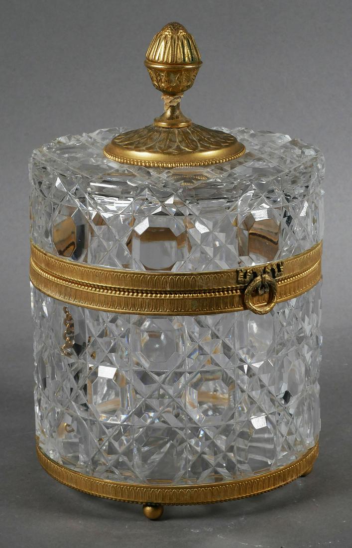 French Gilt Metal and Cut Crystal Lidded Box: Cut crystal cylindrical container and top with gilt decorations, likely Baccarat, etched on bottom Made in France, measures 10 1/2 inches high by 6 5/8 inches in diameter. This item will need to be sh