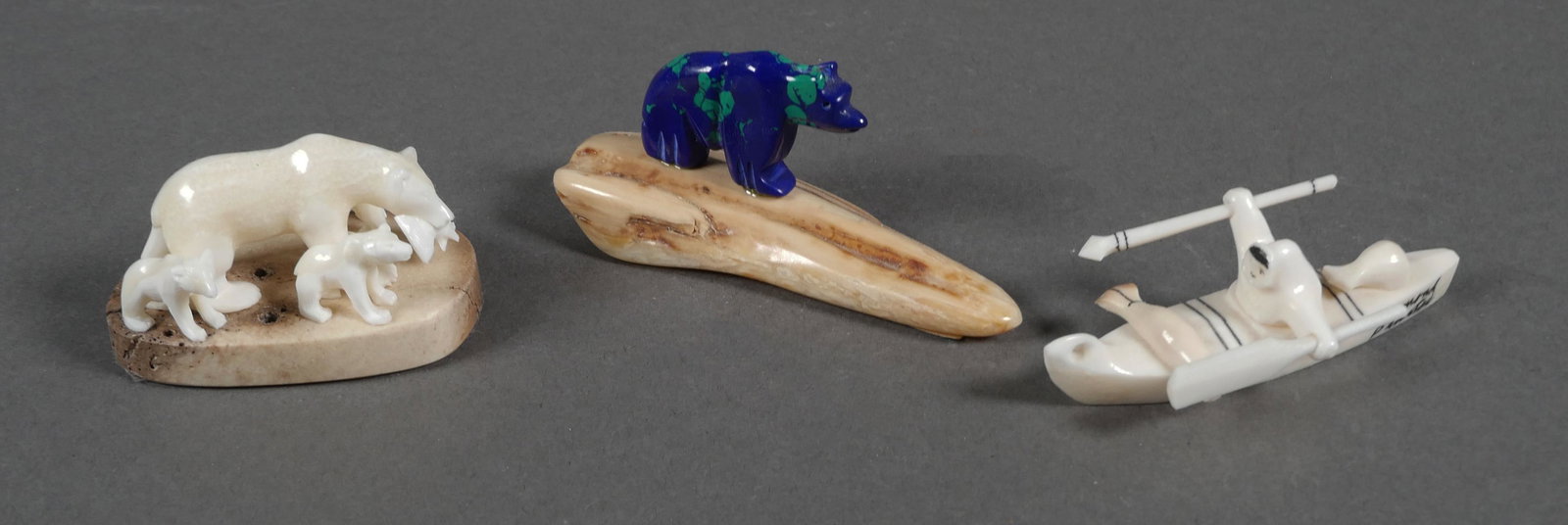 Group of Inuit Carvings: Three carvings of Inuit scenes. The first of a grizzly bear family by Leonard Savage, having a printed label taped to the bottom. The second in the form of a man sitting in a kayak with one seal caugh