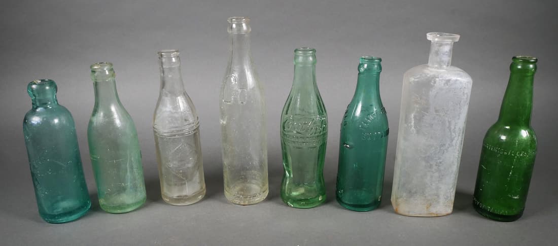 Group of Antique Soda Glass Bottles: Group of 7 soda glass bottles and 1 large druggist glass bottle, largest bottle measures 9" high. Labels include Squeeze, Butterfield Beverage, Coca-Cola Jacksonville bottling, Coca-Cola Ft. Meade, Pe