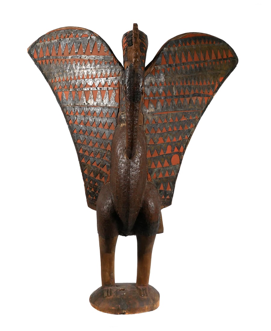 SENUFO HORNBILL SCULPTURE: Carved wood depiction of a bird, body clad with metal and having a geometric triangle pattern of applied metal over red fabric decorating the wings. Life sized figure of a bird with open wings, in the