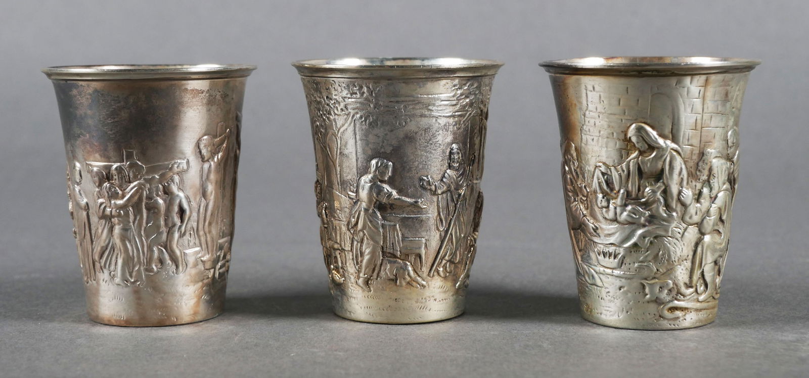 (3) Hanau KARL KURZ Silver Cups: Three antique silver communion (or shot) cups by German silversmith Karl Kurtz. Each cup has a repousse biblical or religious scene. Hanau hallmarks, shot size, approx. 2" tall. Overall weight 3.15 oz