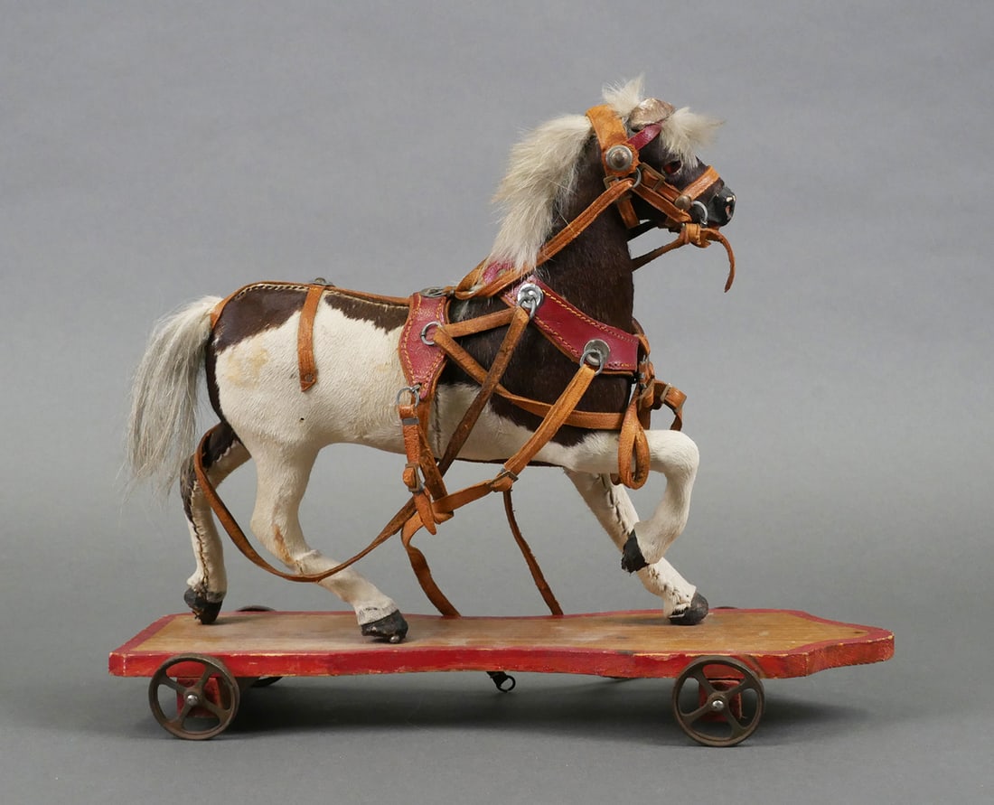 Antique Horse Pull Toy: Antique child's pull toy. Galloping or trotting spotted horse mounted on a wood platform with metal wheels. Horse is covered in natural animal hide of white and brown with a fur mane and horsehair tai
