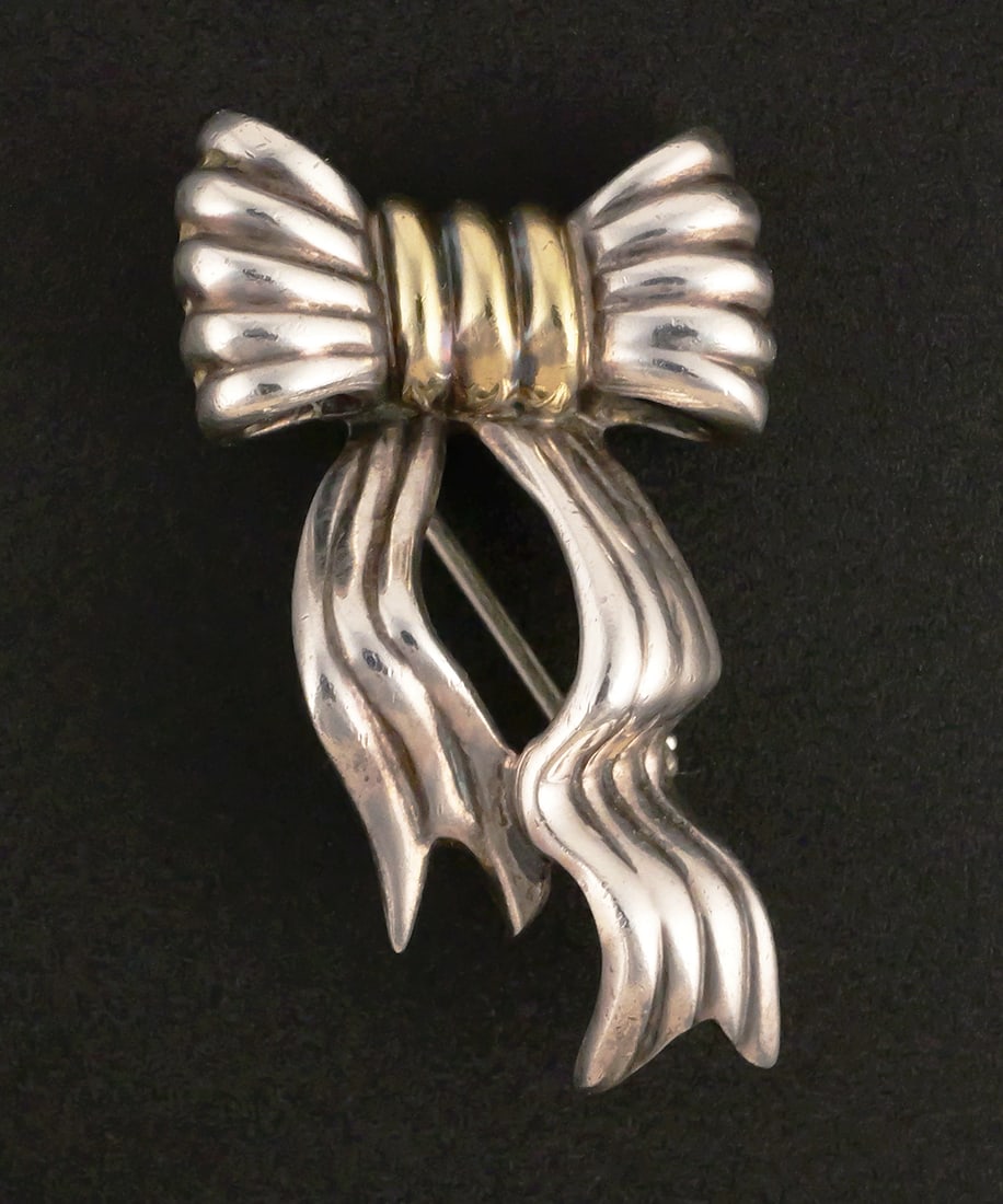 TIFFANY Sterling & 18k Gold Pin: Tiffany & Co. sterling silver accented with 18 karat yellow gold bow shape brooch. Marked 925 and 750 (18 k), 5.1 grams tw, approx. 1-1/8"L. This item can be shipped in-house. Multiple lot combined sh