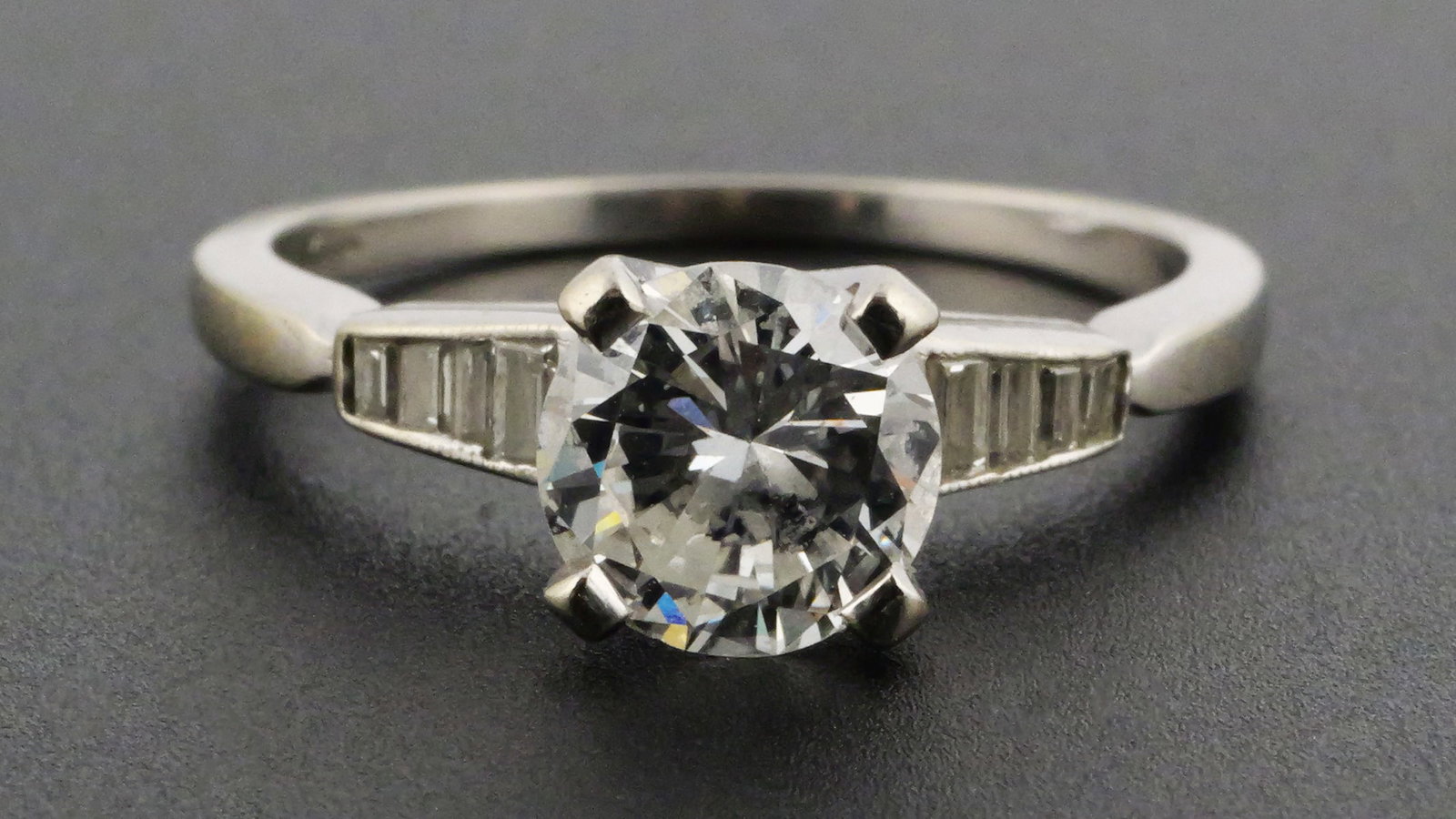 14K White Gold Ring, .84 Carat Diamond: White gold ring with round brilliant .84 carat diamond, VS2 clarity, I color. Diamond is flanked by eight baguette diamonds, about .20 cttw, G color and VS clarity. Total weight 2.5 grams. Size