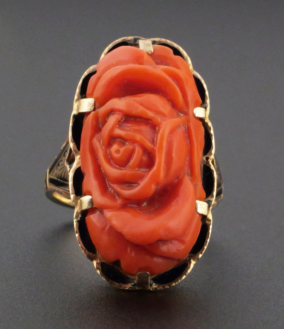 14K Gold Carved Coral Rose Ring: 14K yellow gold enameled ring set with an elongated cameo, oval orange-red coral carving depicting a dimensional rose blossom and foliage, held by multiple tabs in an open-backed setting. Antique