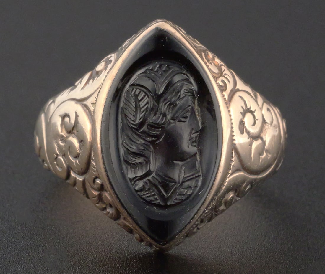 Antique 9K Gold Classical Intaglio Ring: Antique 9K gold ring set with a marquise-shaped onyx stone intaglio carved with a classical female profile. Ornately engraved shoulders with scrolling foliate decoration. Overall weight 3.9 grams.