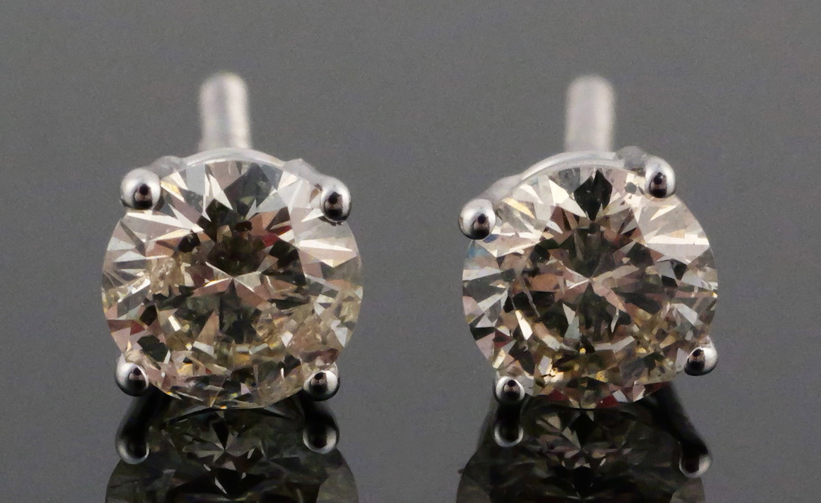 14k White Gold One Carat Diamond Earrings: Pair of white gold earrings, each set with a half-carat diamond. Total combined weight 1.1 grams. This item can be shipped in-house. Multiple lot combined shipping may require 3rd Party shipping.