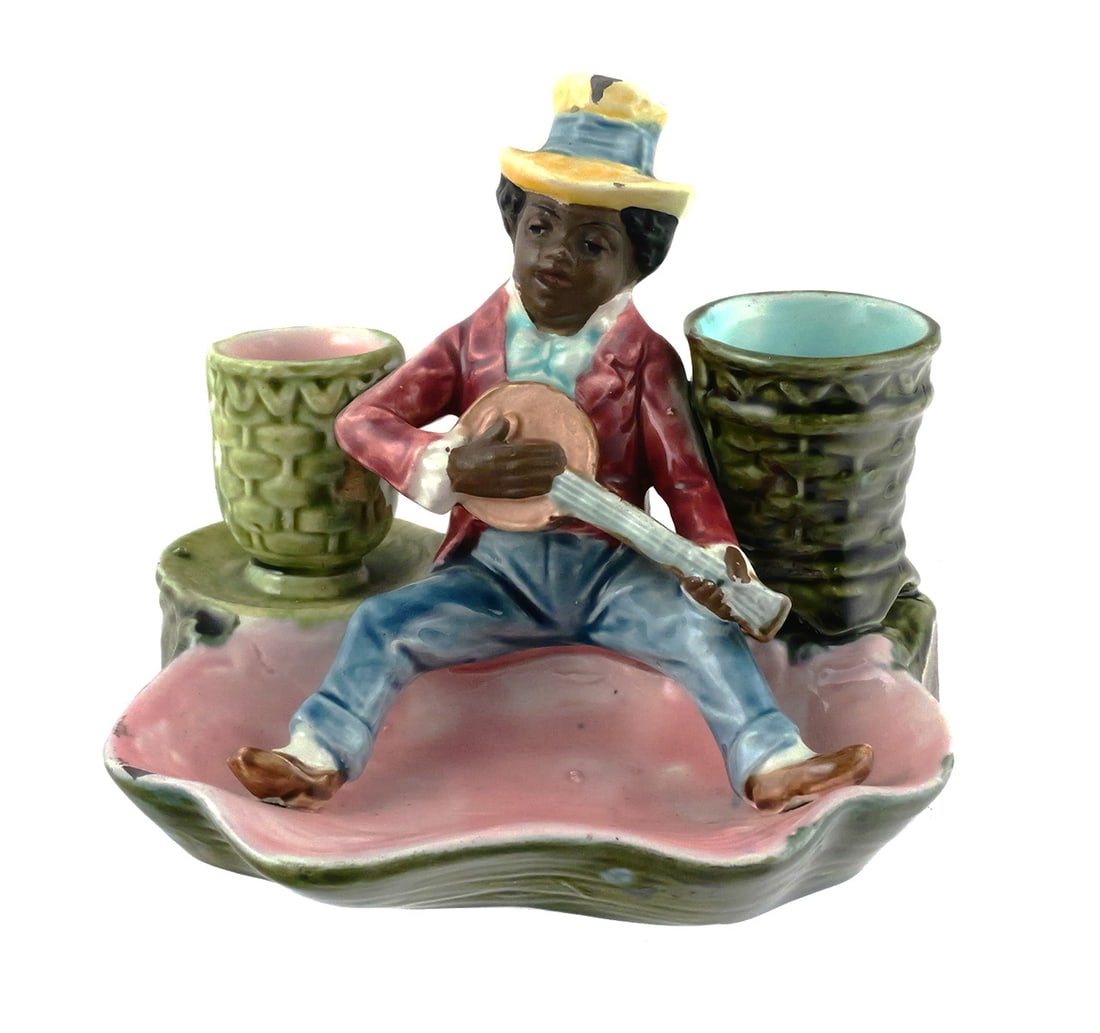 Majolica Blackamoor Banjo Picker Striker & Tray: Majolica Blackamoor Banjo Picker Match Holder Striker & Tray. There are two barrels to hold matches. The back side of the small barrel has a spot for striking matches. Measures approx 4-1/2" tall,