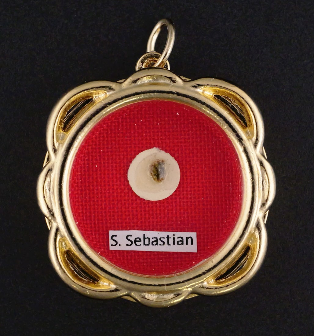St. Sebastian Reliquary Theca: First class ex ossibus bone fragment relic of Saint Sebastian, patron saint of athletics. Wax seal intact. Housed in a gold metal glass front reliquary theca with loop for hanging. Approx. 1-3/8"