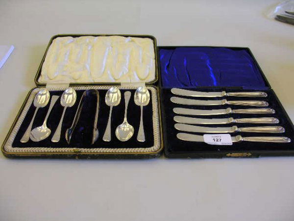 A cased set of six shell and thread pattern butter: A cased set of six shell and thread pattern butter knives, Sheffield, 1917 together with a matched set of six Hanovarian pattern teaspoons and sugar tongs in a fitted case, engraved with initials, She