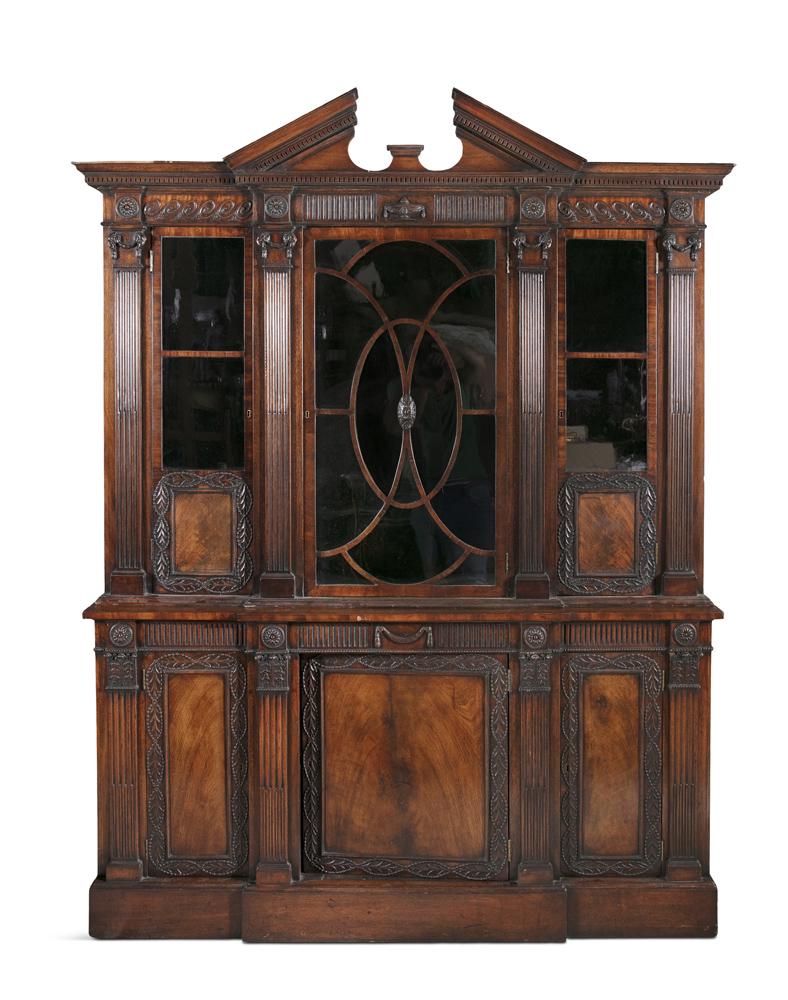 A MAHOGANY BREAKFRONT BOOKCASE, following a design by: A MAHOGANY BREAKFRONT BOOKCASE, following a design by William Kent, surmounted by an architectural pediment, above three glaze panel doors, with intertwined ovals and divided by reeded pilasters, and